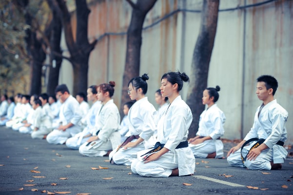 A group of people in white uniforms sitting on the ground.